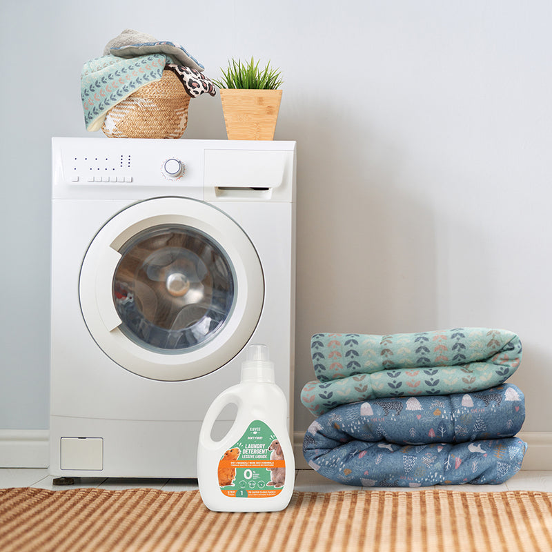 Un bidon de lessive liquide de la marque Kavee au pied d'une machine à laver avec du linge propre autour