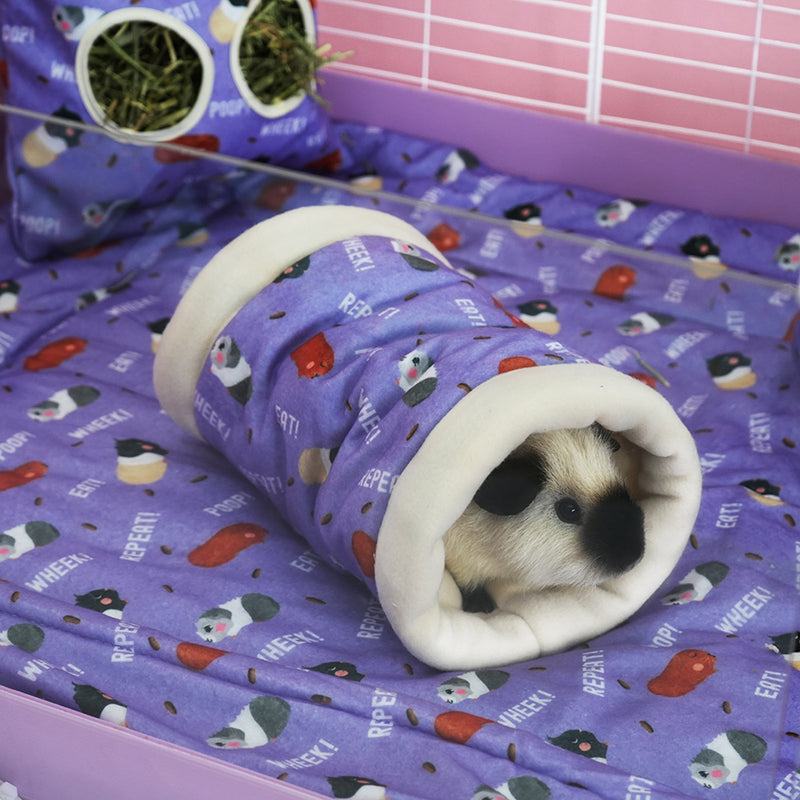 cochon d'inde caché dans un tunnel violet aux motifs caca de la marque Kavee dans une cage sur un tapis avec un sac à foin